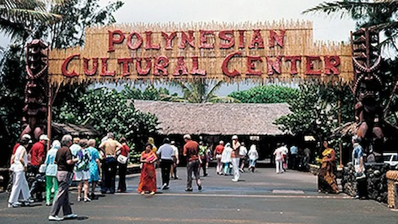 Old entrance sign to the Polynesian Cultural Center, with a large tiki statue on each side.