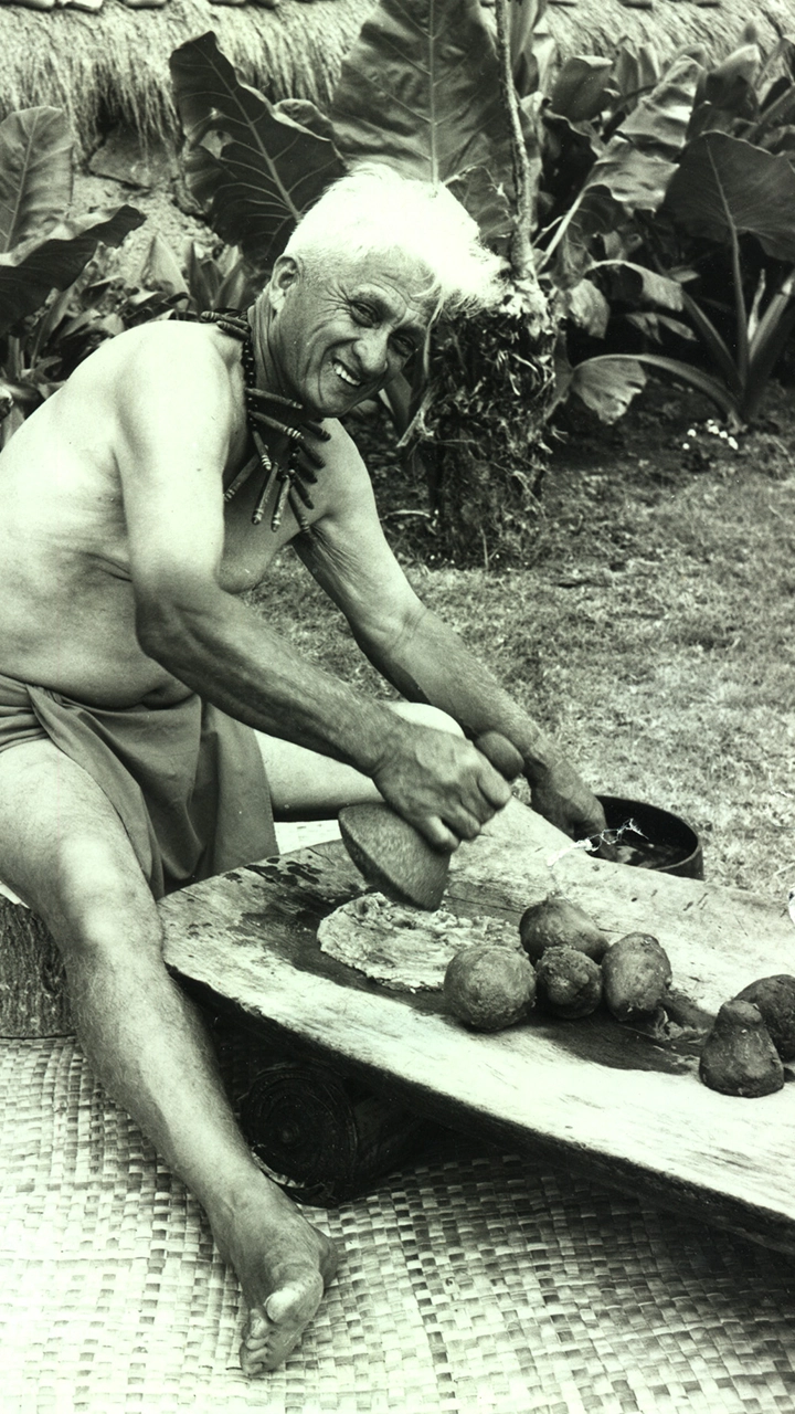 Black and white historical image showing a Polynesian man pounding poi