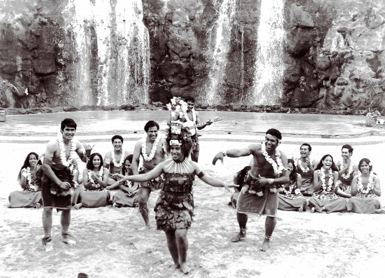  Male and female dancers in Tongan dress, performing in front of a waterfall.