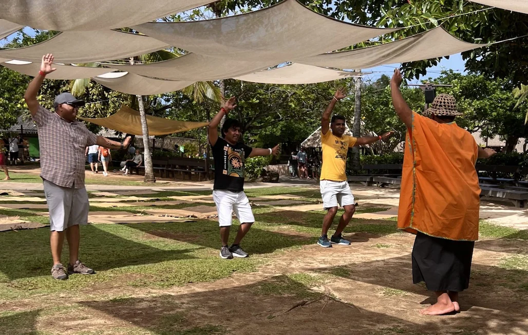 Under billowing canopies, a male worker teaches 3 male guests to dance.