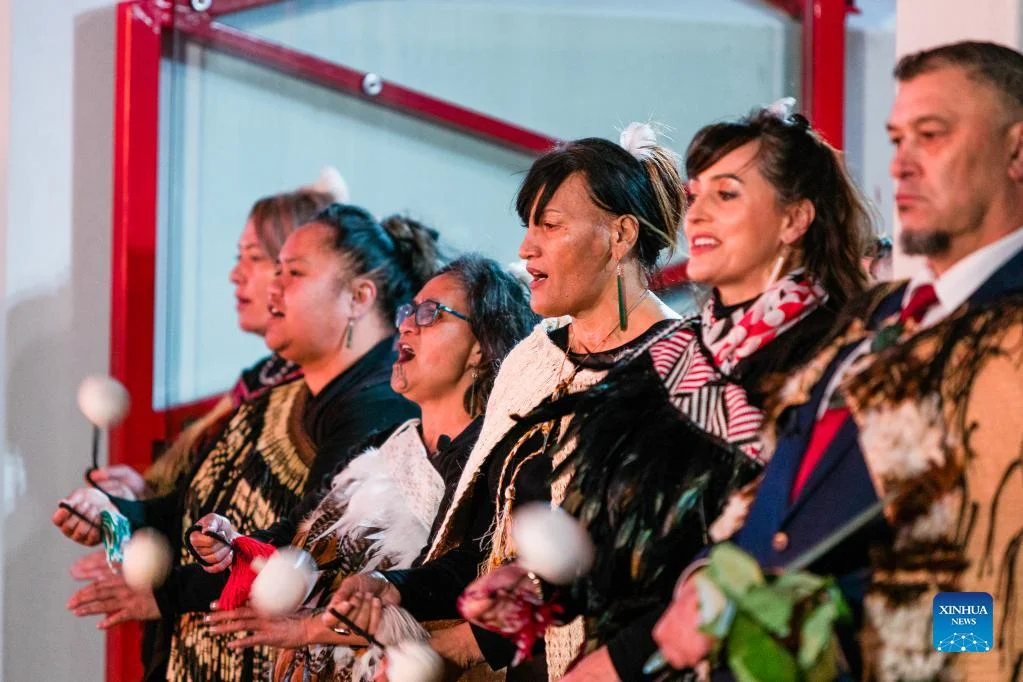 Maori men and women, dressed in traditional attire, proudly singing while spinning poi balls for a New Years celebration.
