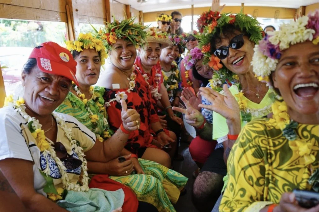 Happy Tahitian women with brightly colored flower crowns on a bus.