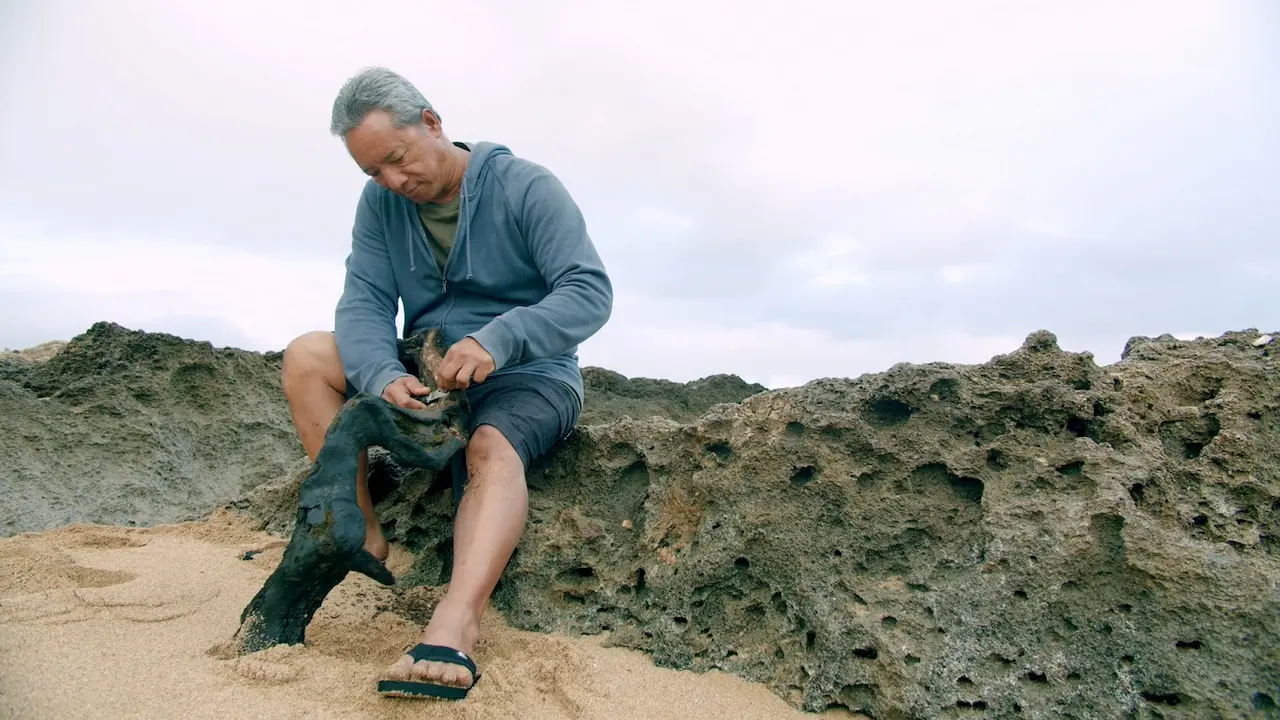 Kawika Eskaran as he works with a branch by the sea.
