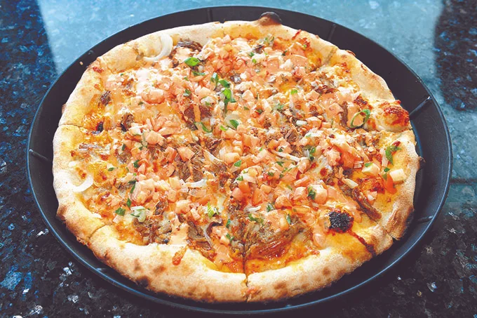 A large pizza stopped with lomi salmon and kalua pork.