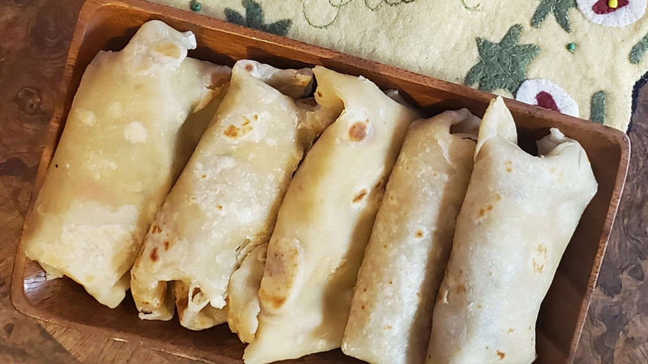 Rectangle acacia wood plate with five Fiji chicken curry wrapped in roti sitting atop a hot pad saying aloha and a wooden table.