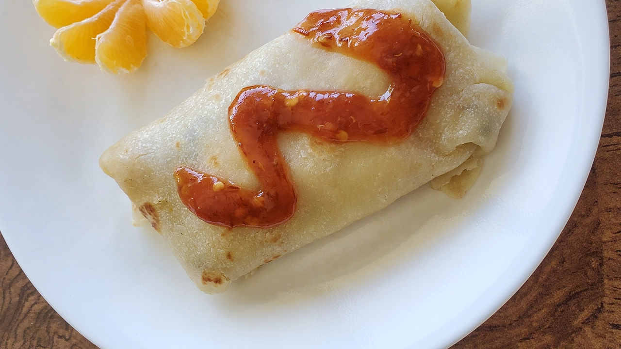 White plate and of flat bread stuffed with chicken curry topped with hot sauce