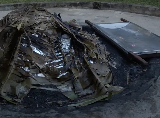 Charred leaves and tinfoil on top of a traditional earth oven.
