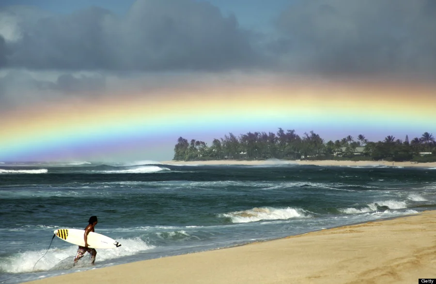 Hawaii, Oahu, North Shore, Surfer exiting water admires a beautiful, bright rainbow. Photo courtesy of Huffington Post